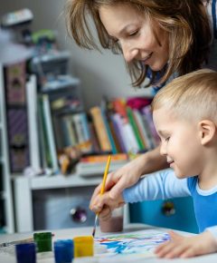 Young adult mom and cute little blond kid boy enjoy have fun painting with watercolor brush bright